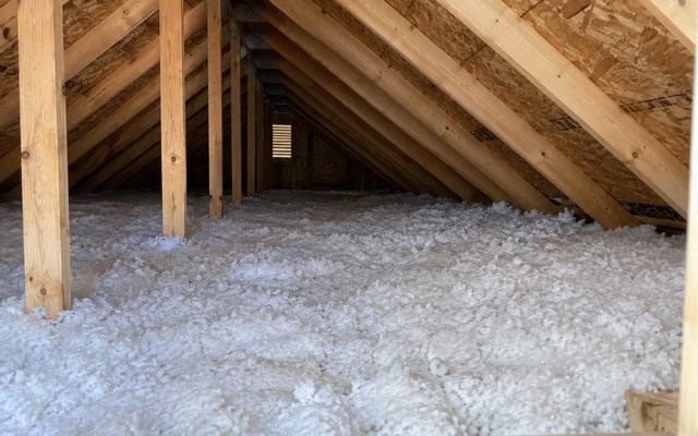 Thick white loose fill between wooden posts and roof trusses in a long attic
