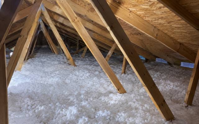 White loose fill spread around the angled braces of an attic truss system