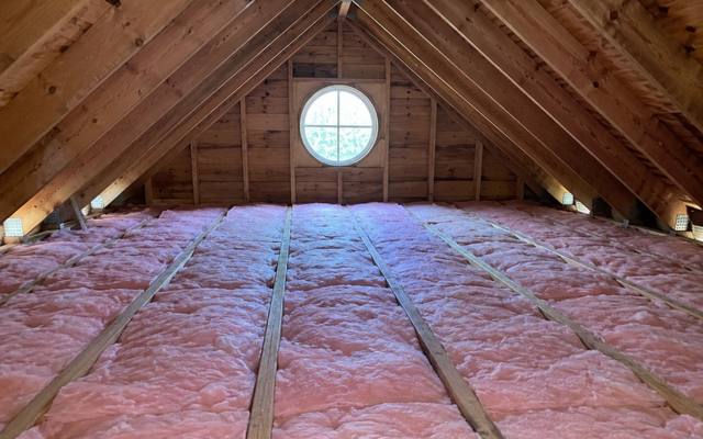 Pink batts laid in rows across a wide attic floor under a gable with a round window